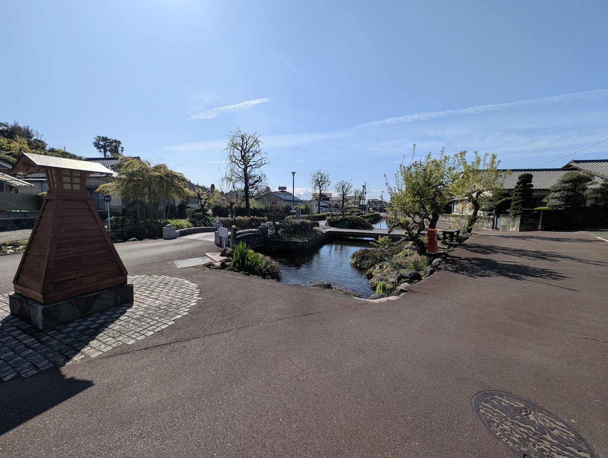 泉の郷湧水公園の入り口付近。木製の灯篭と澄んだ水路にかかる石橋がある、のどかな風景。